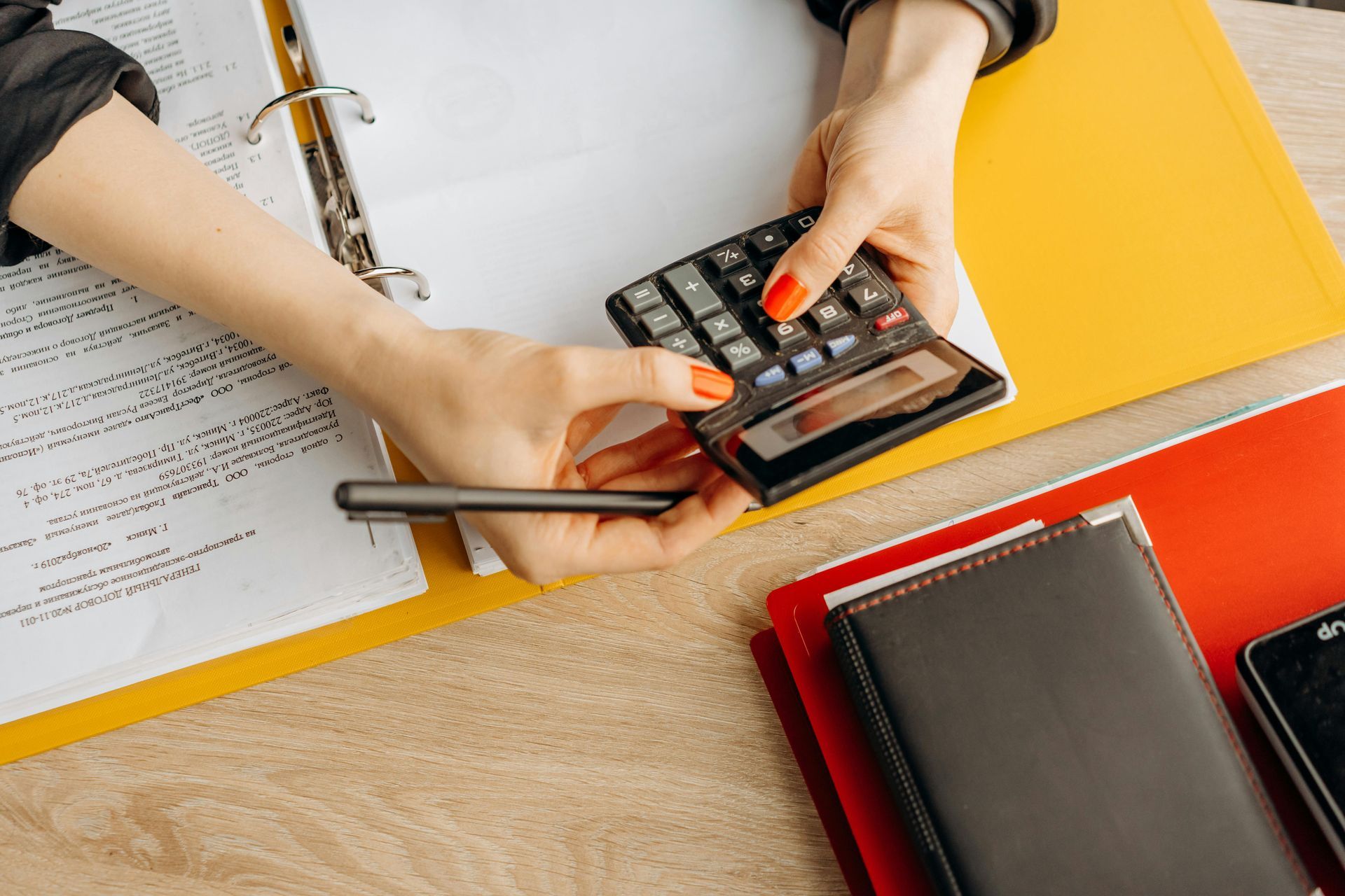Hands using calculator with pen and papers on a desk.