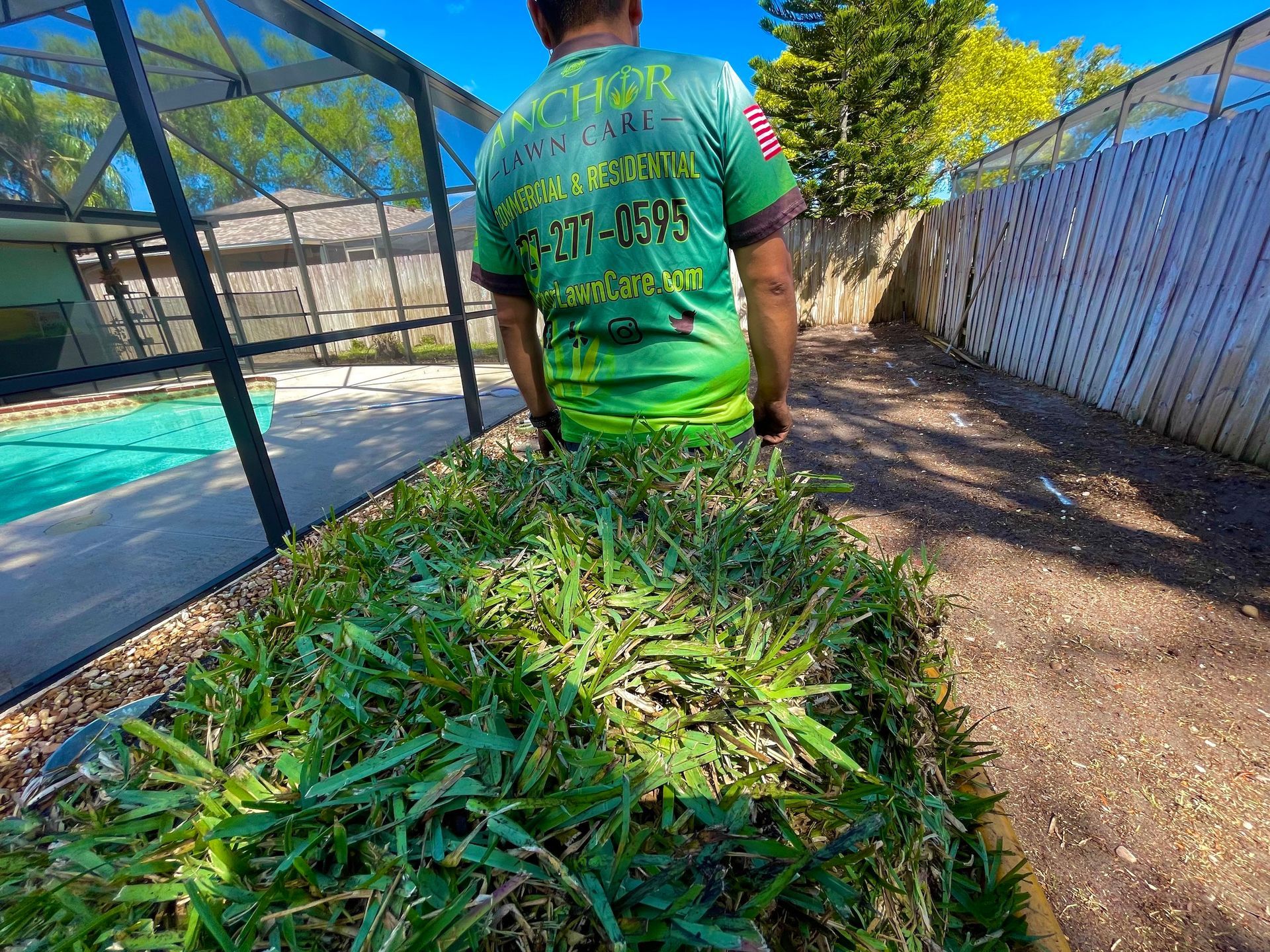 A man in a green shirt is standing next to a pile of grass.