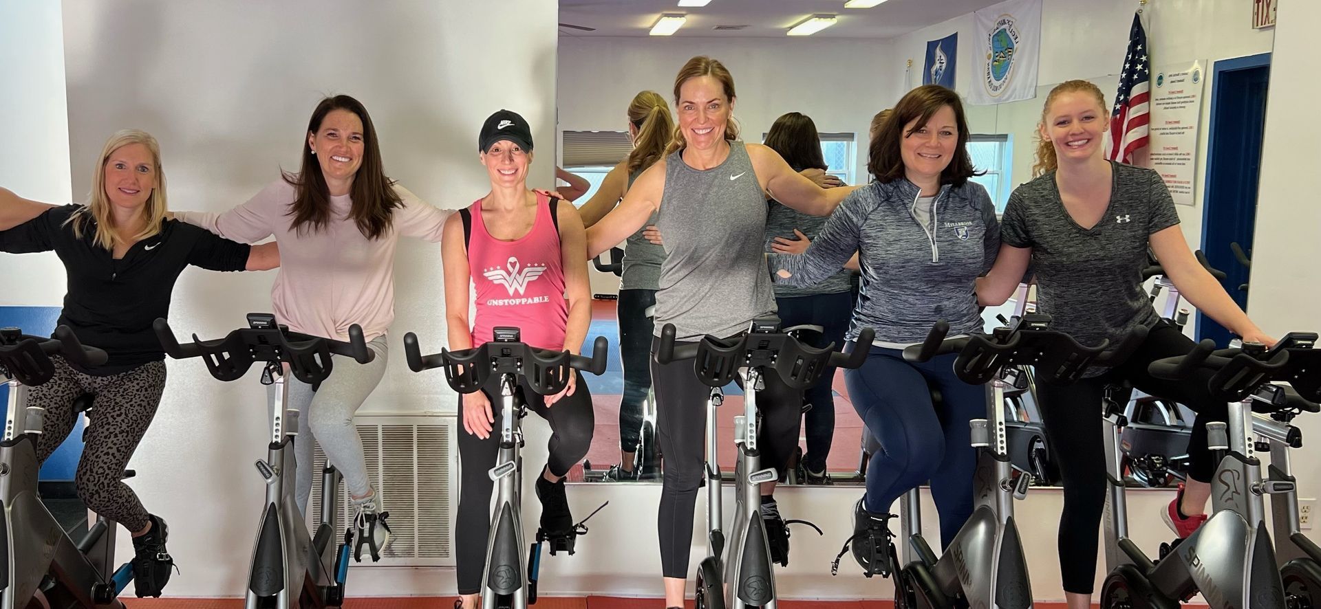 A group of women are standing next to each other on exercise bikes in a gym.