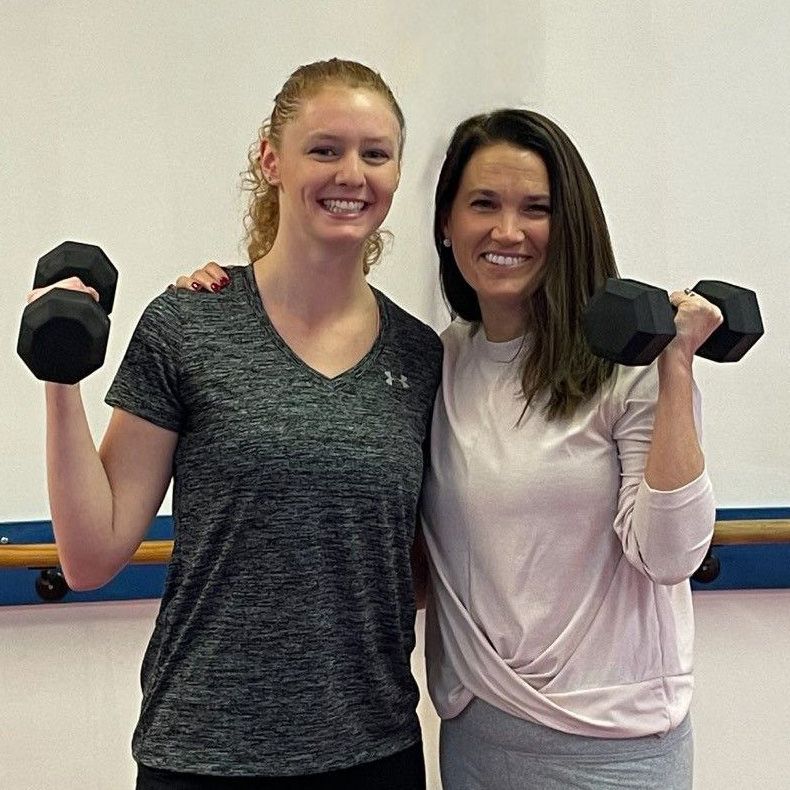 Two women are posing for a picture while holding dumbbells.