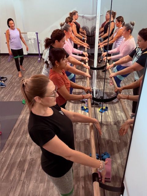 A group of women are doing stretching exercises in front of a mirror.