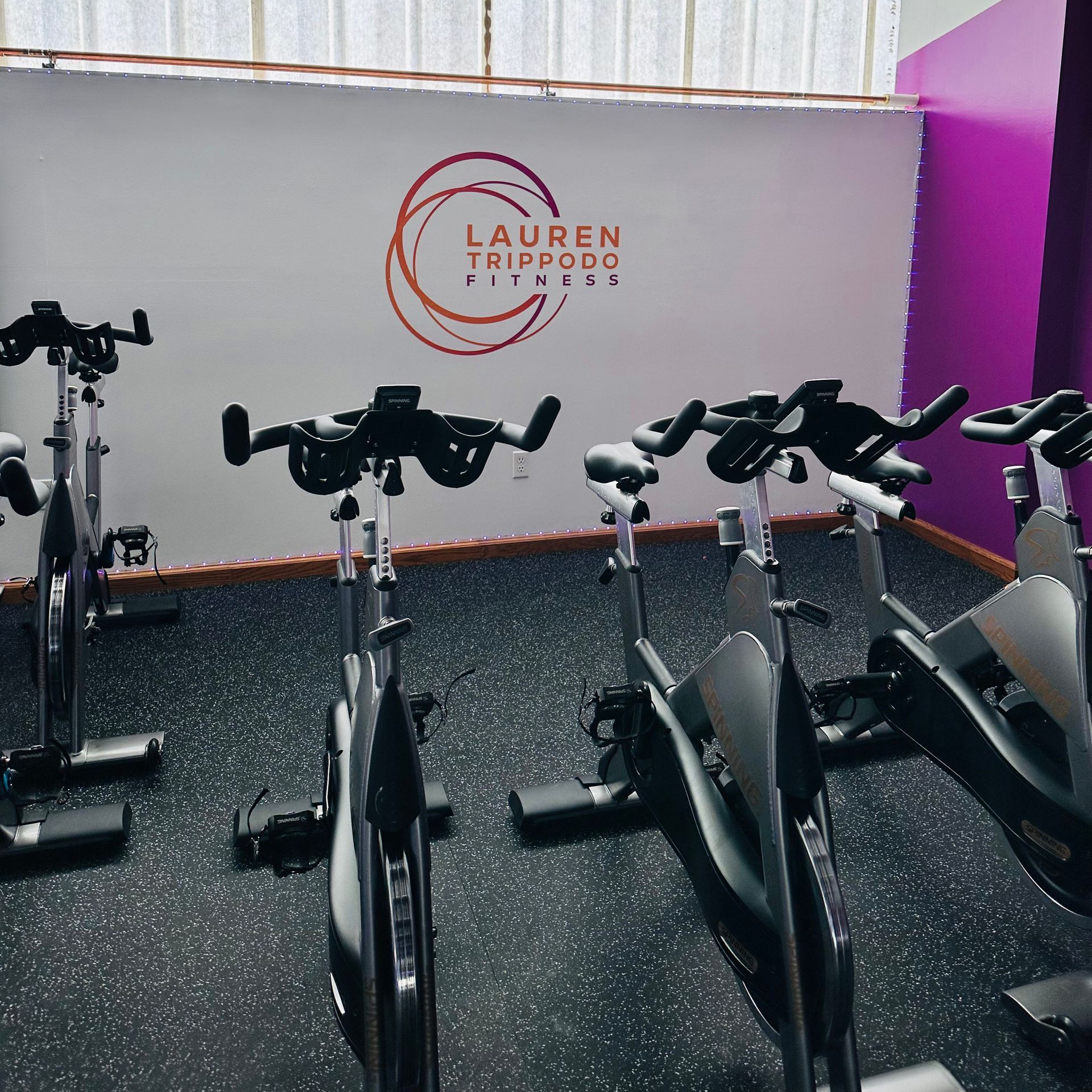 A row of exercise bikes are lined up in a room with a wall that says Lauren Trippoo Fitness.