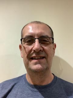 A man wearing glasses and a blue shirt is smiling for the camera.