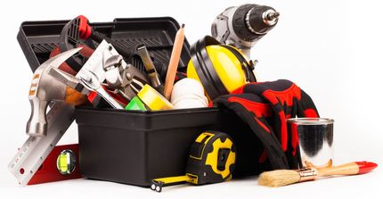 A black toolbox overflowing with various tools, including a hammer, drill, measuring tape, and paint can.