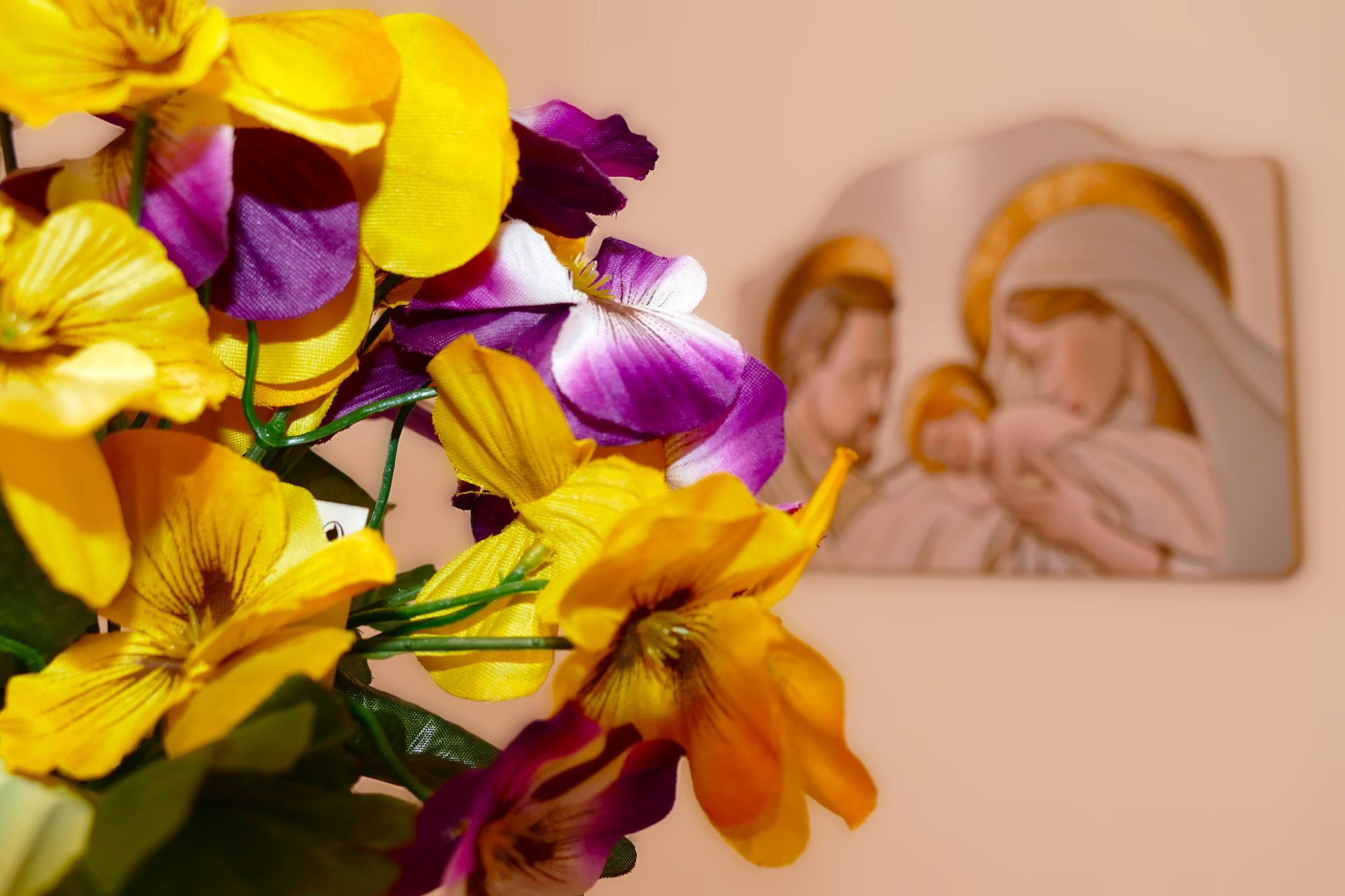 A bunch of yellow and purple flowers with a picture of jesus and mary in the background