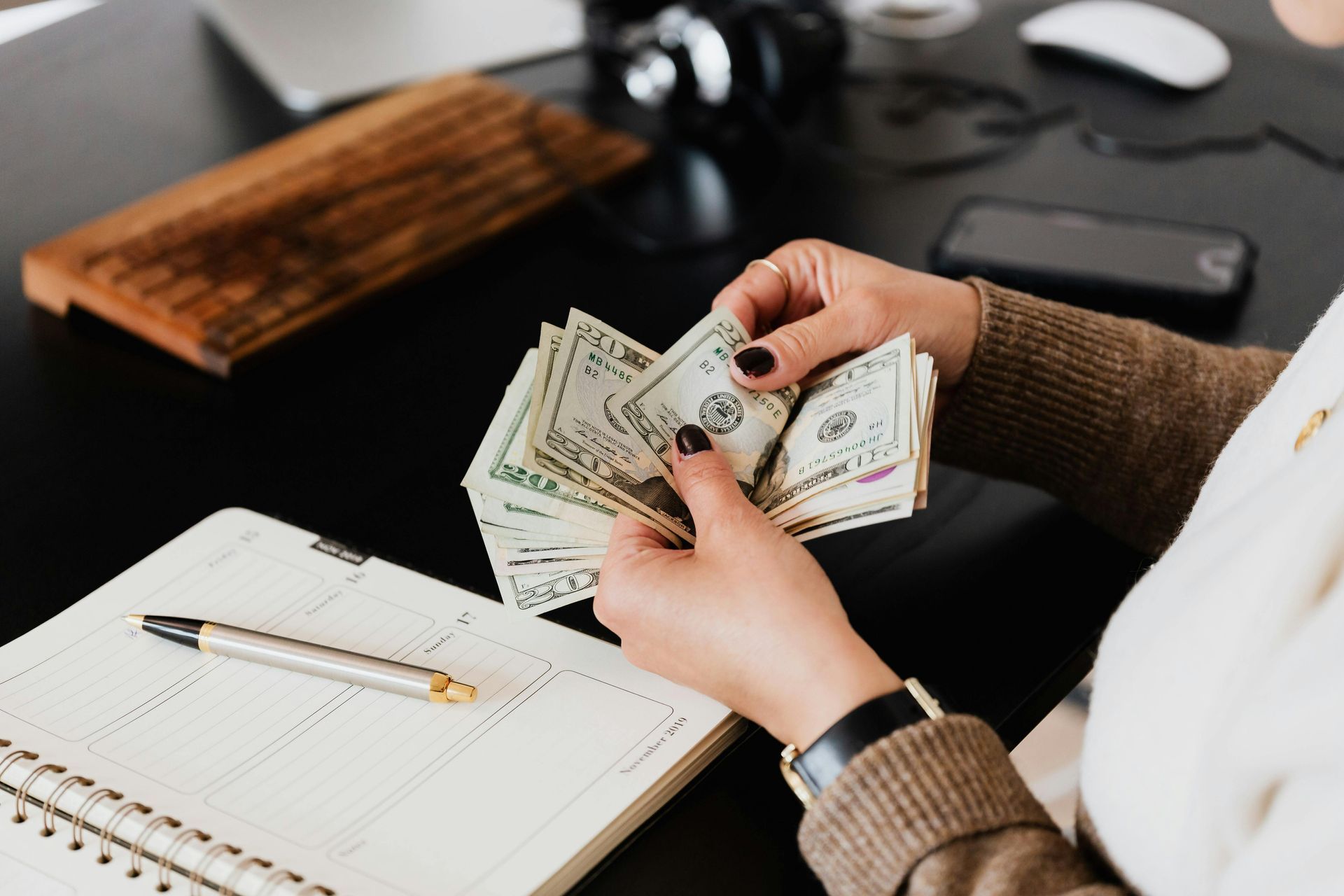 Person counting money over an open notebook. US dollar bills are held in the hands.