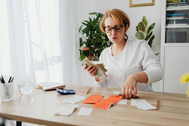 Woman counting cash at a desk, surrounded by bills and financial documents.