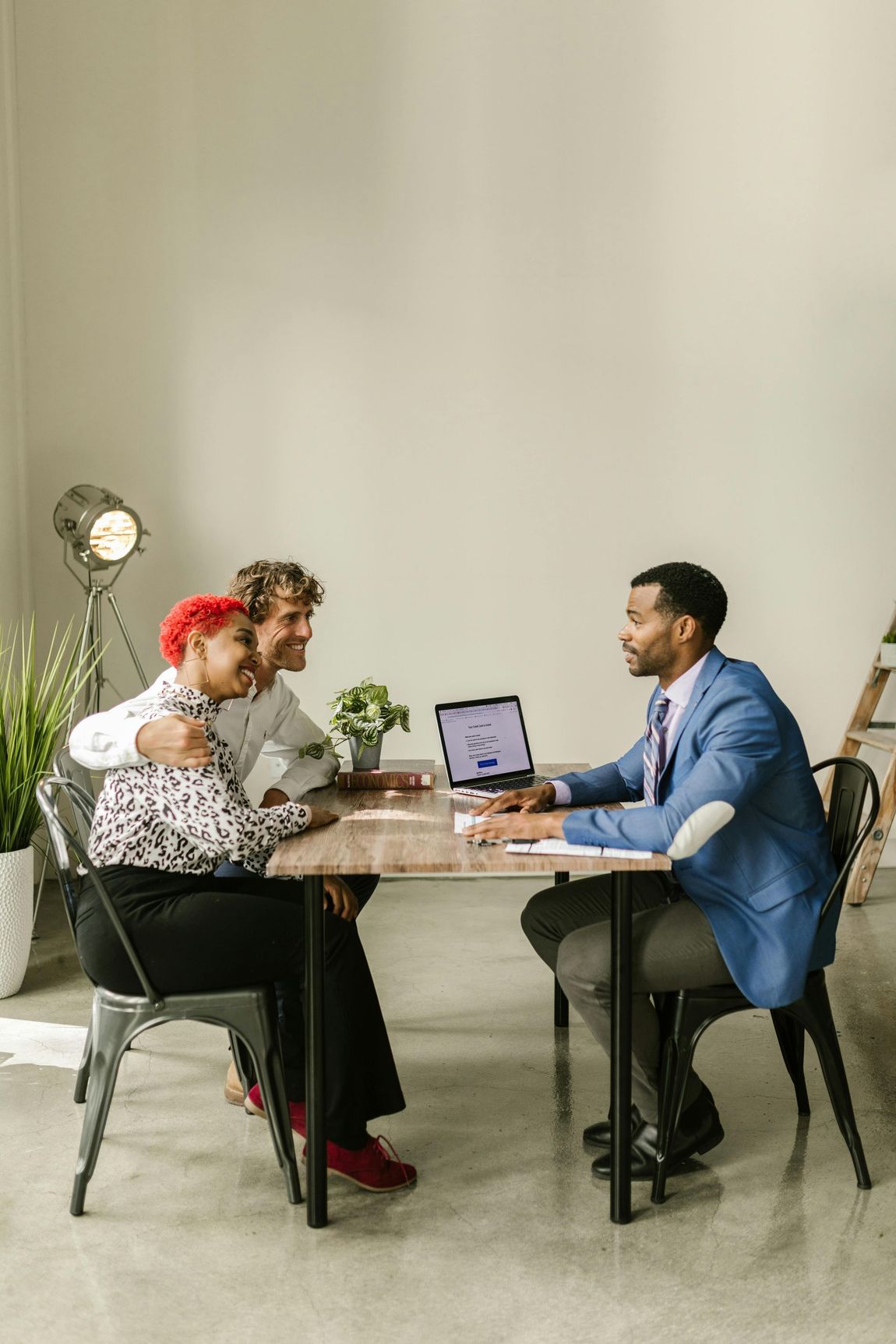Couple embracing at a table with a professional, looking at a laptop.