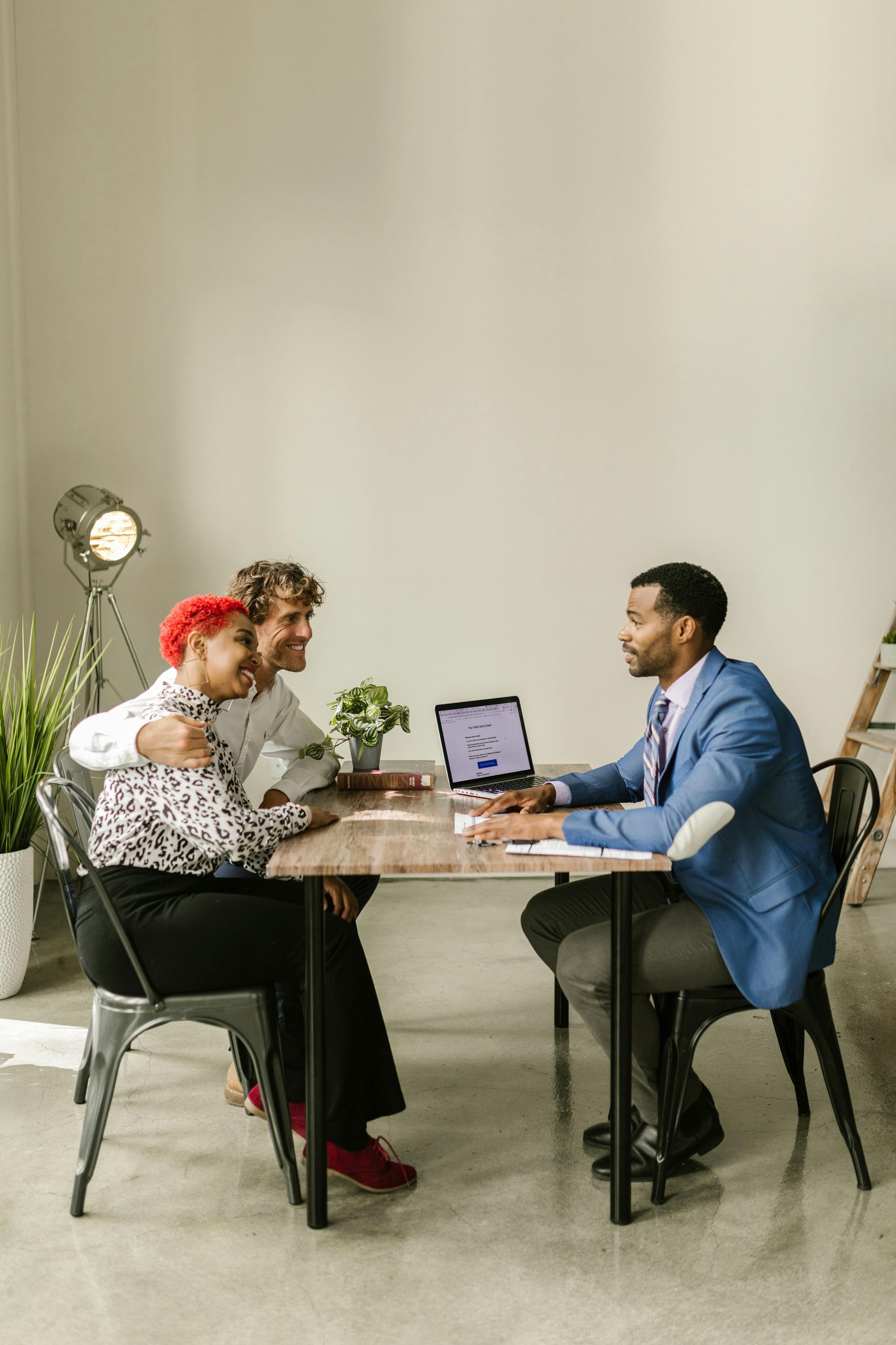 Couple embracing at a table with a professional, looking at a laptop.