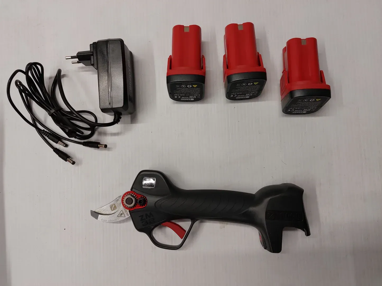 Una cesoia a batteria con tre batterie e un caricabatterie