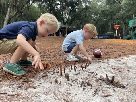 Two boys playing with sticks in the sand on playground.