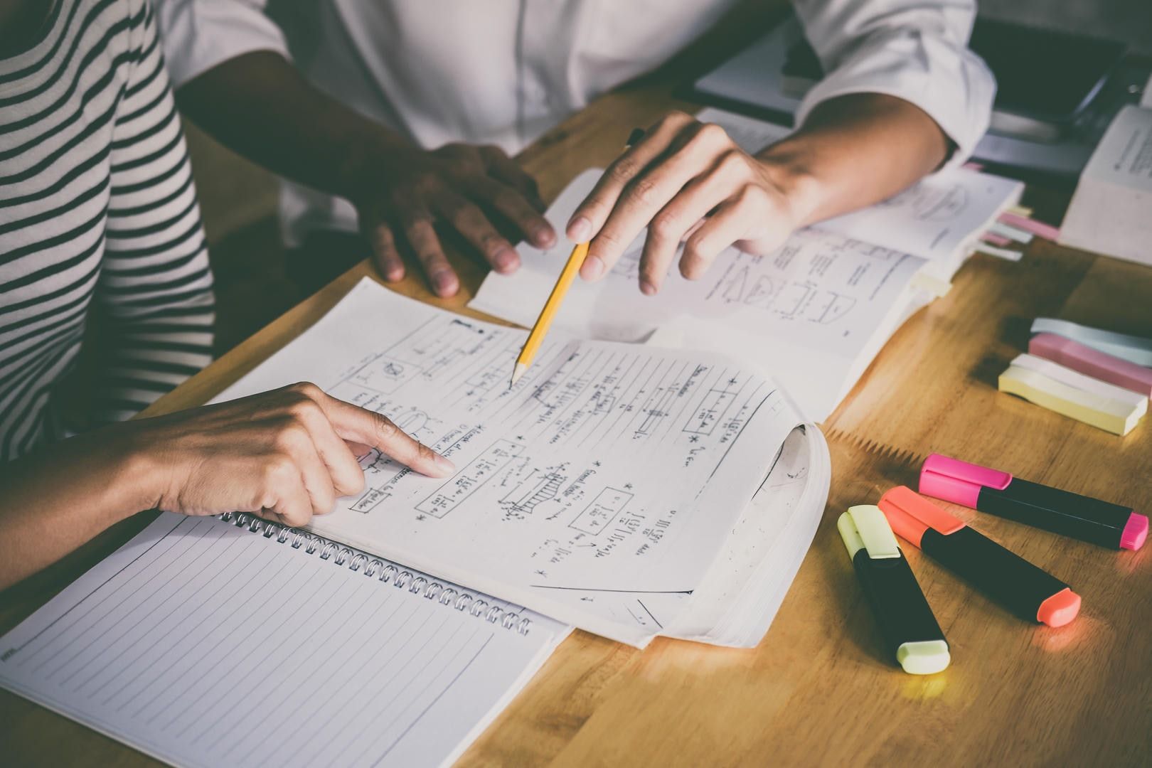 Two people studying together at a desk, pointing at handwritten notes.