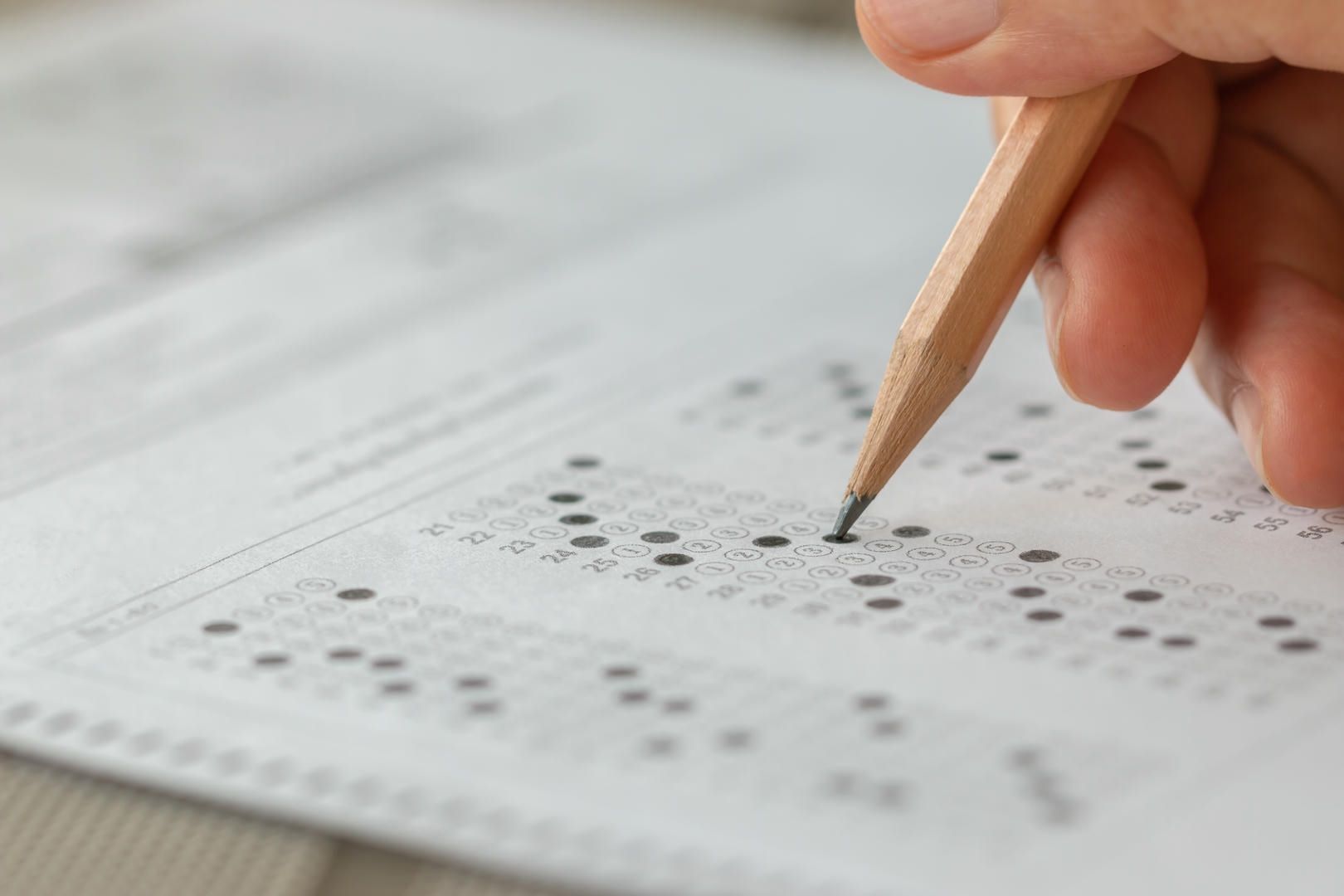 Hand holding a pencil filling in a bubble answer sheet for a test.