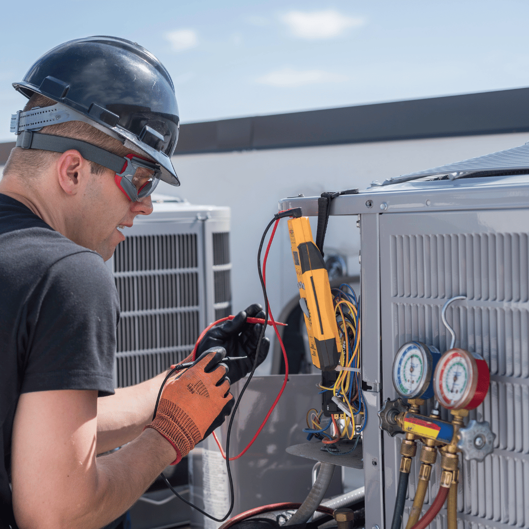 A man wearing a hard hat and goggles is working on an air conditioner.