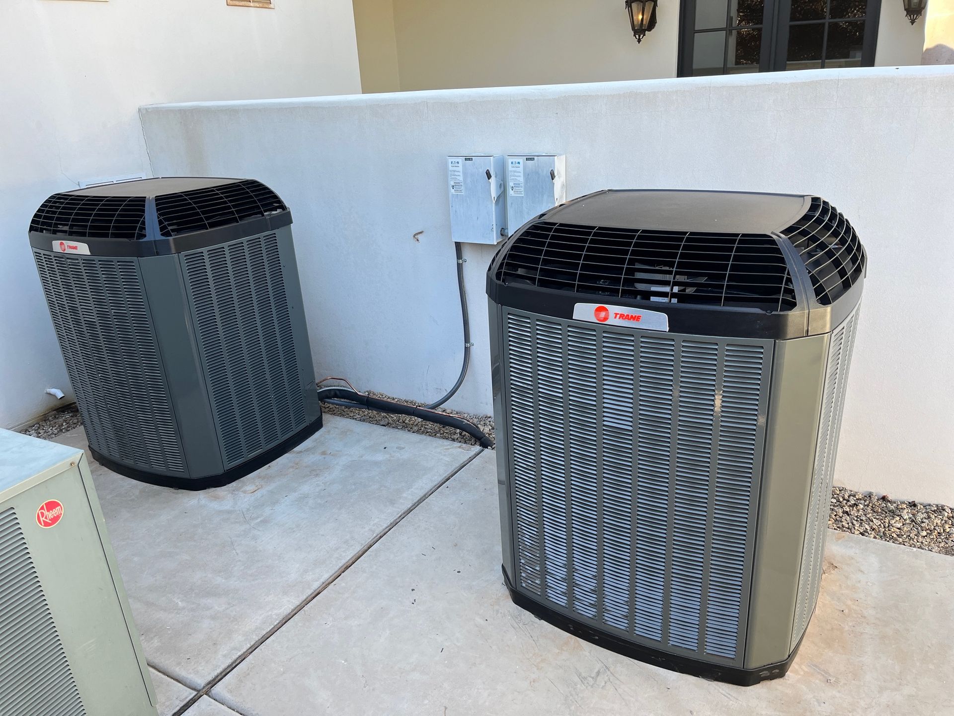 Two air conditioners are sitting next to each other on a sidewalk.