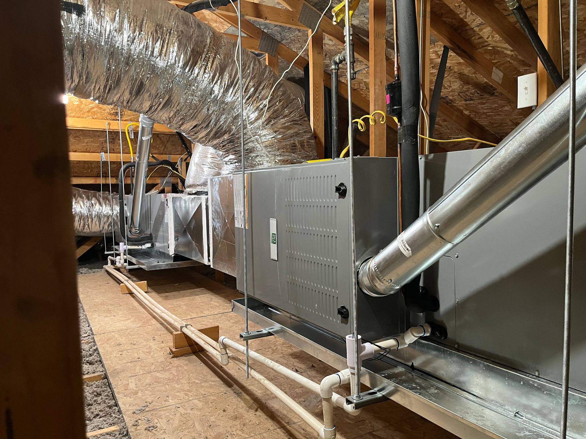 There are a lot of pipes hanging from the ceiling in the attic.