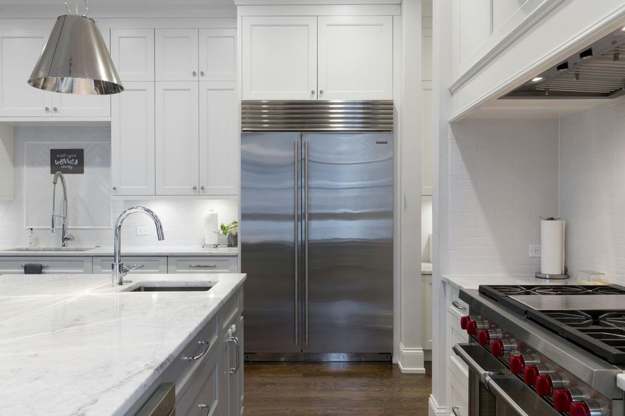 Stainless steel refrigerator in a white kitchen, with a granite countertop and gas stove.