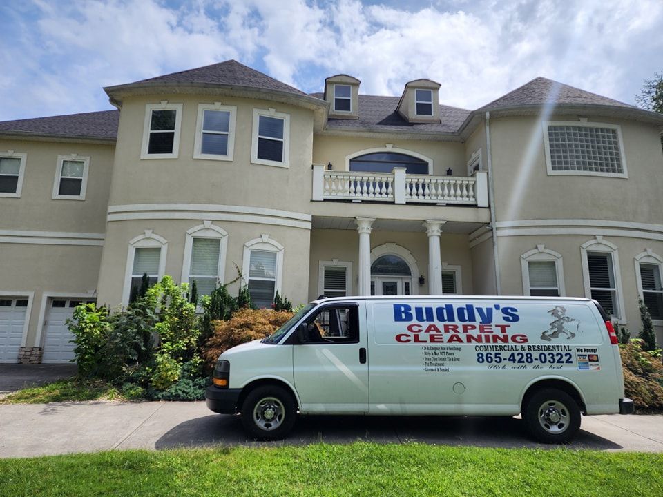 A buddy 's carpet cleaning van is parked in front of a large house
