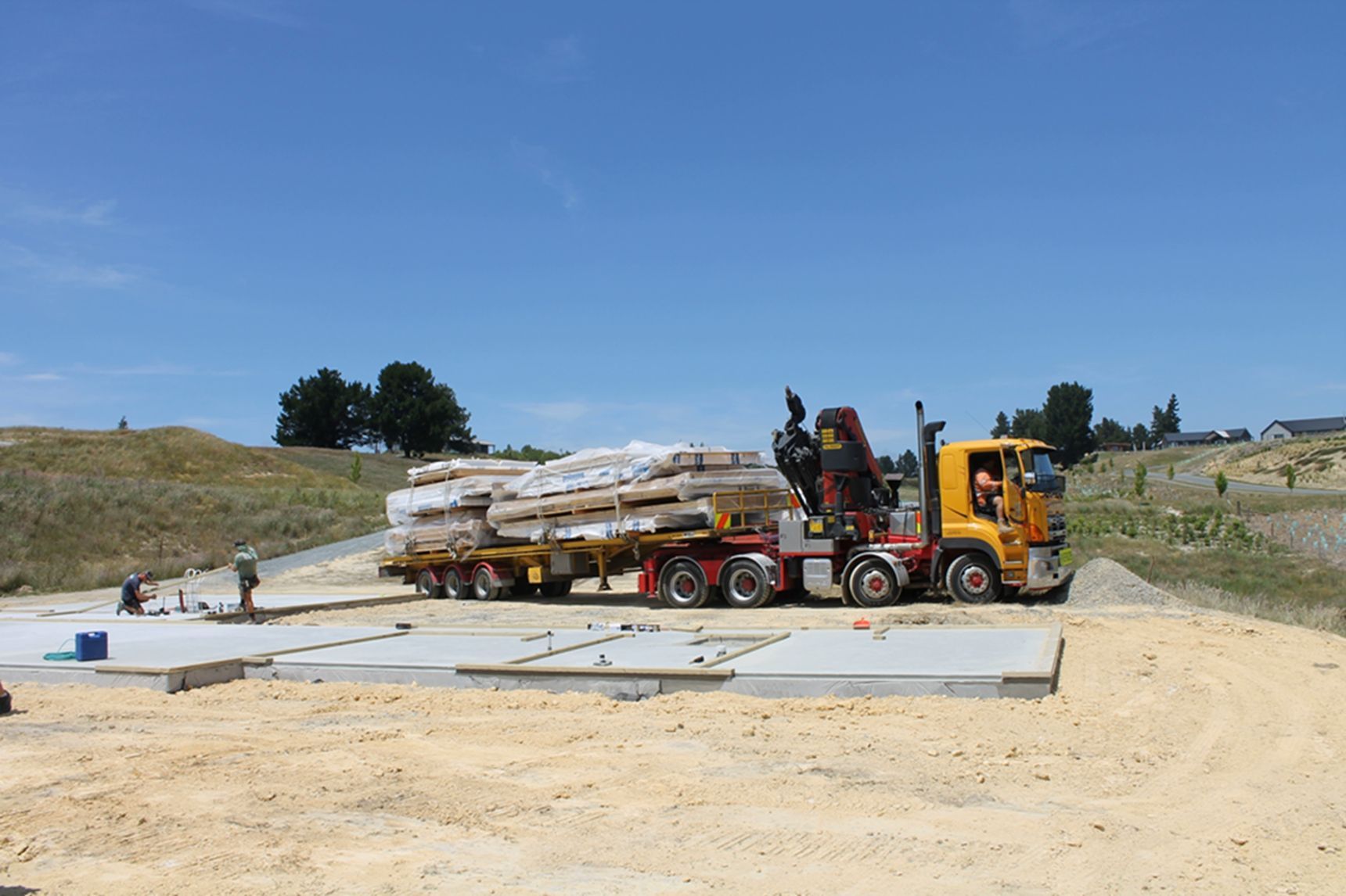 A yellow truck is carrying a trailer full of wooden boards.