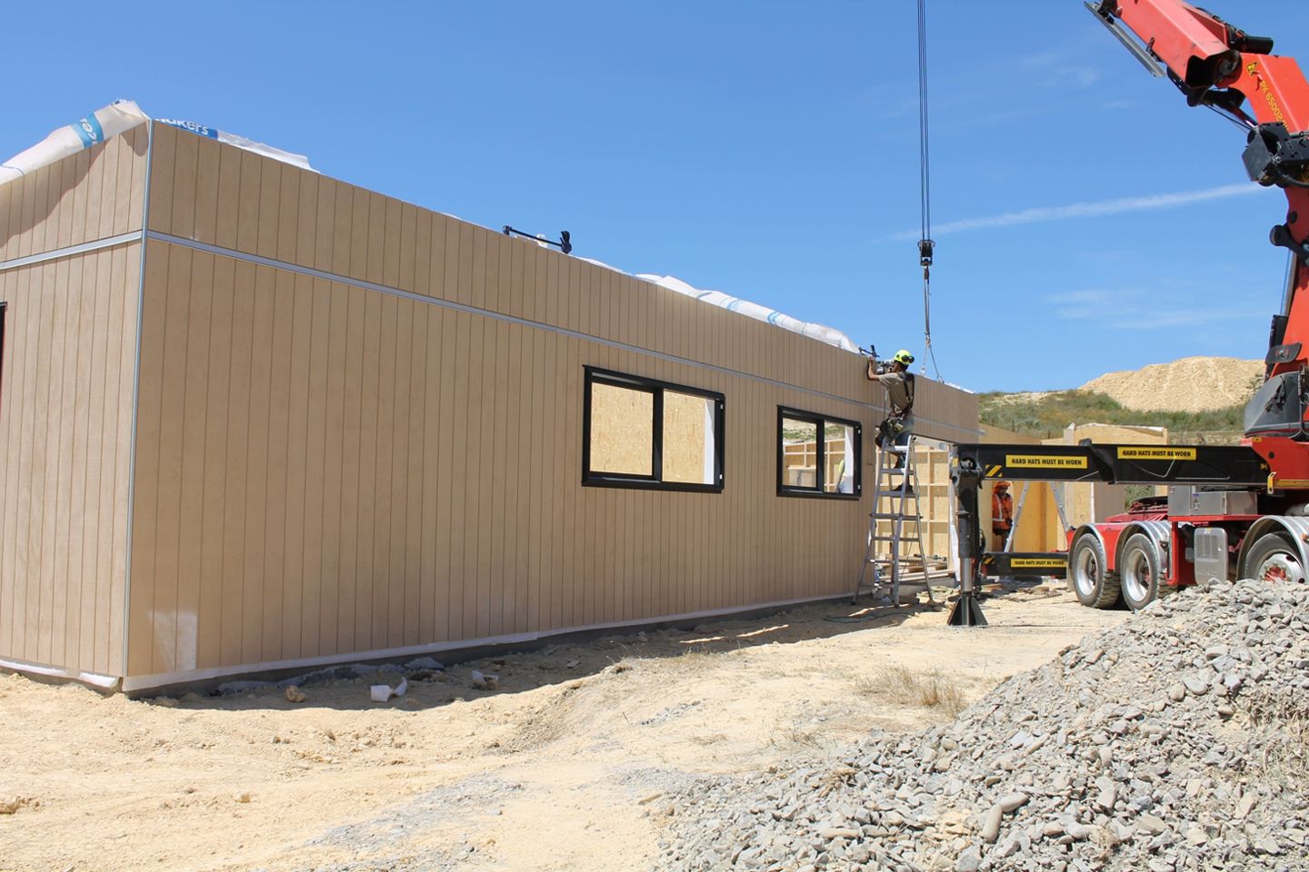 A crane is lifting a piece of wood on top of a building.