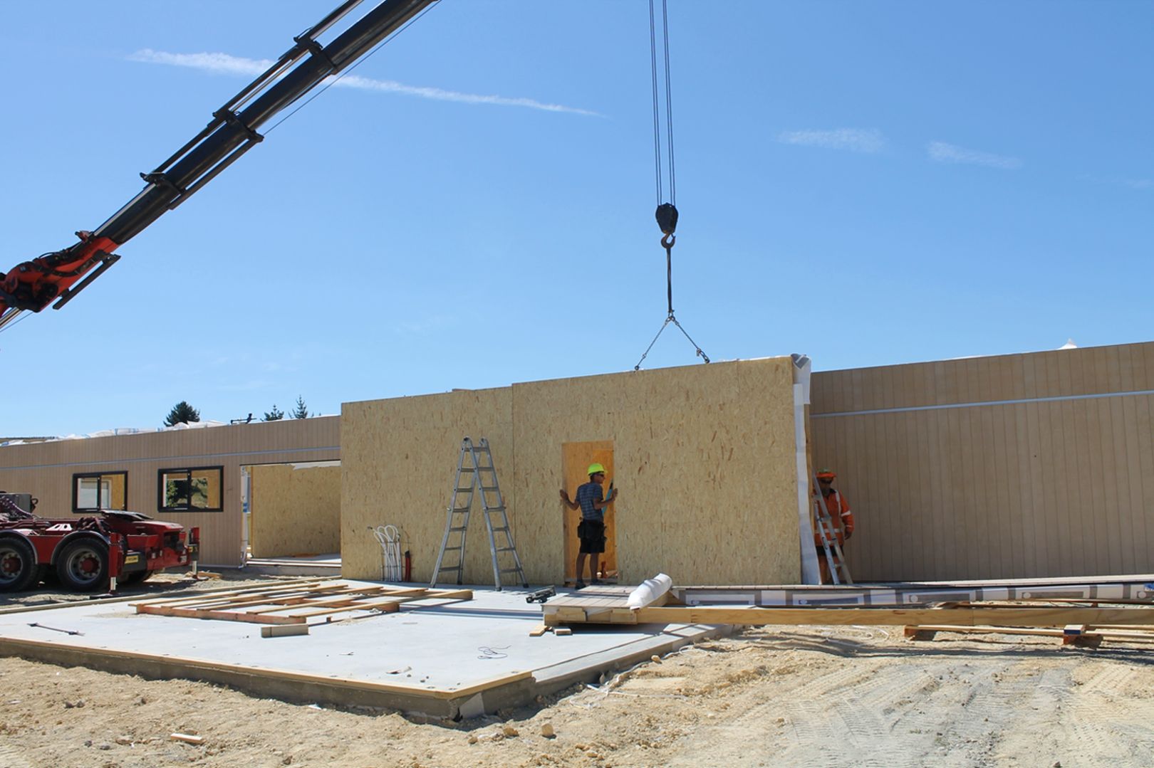 A crane is lifting a wooden wall in a construction site