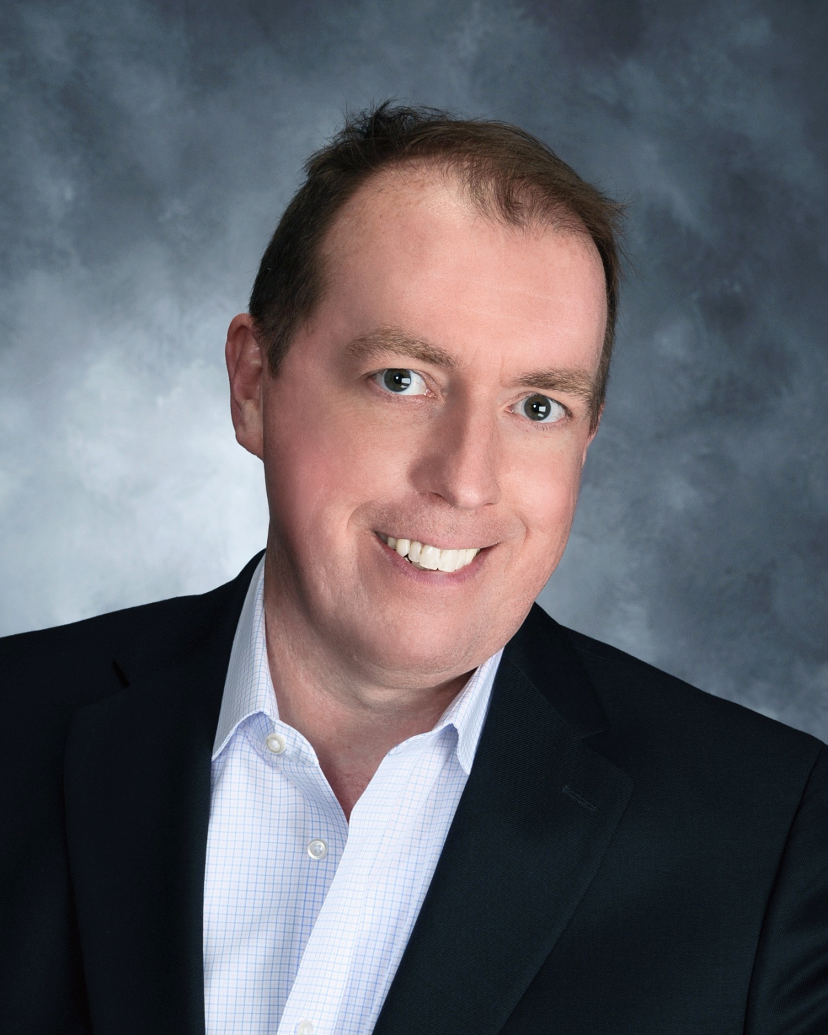 A man in a suit and white shirt is smiling for the camera.
