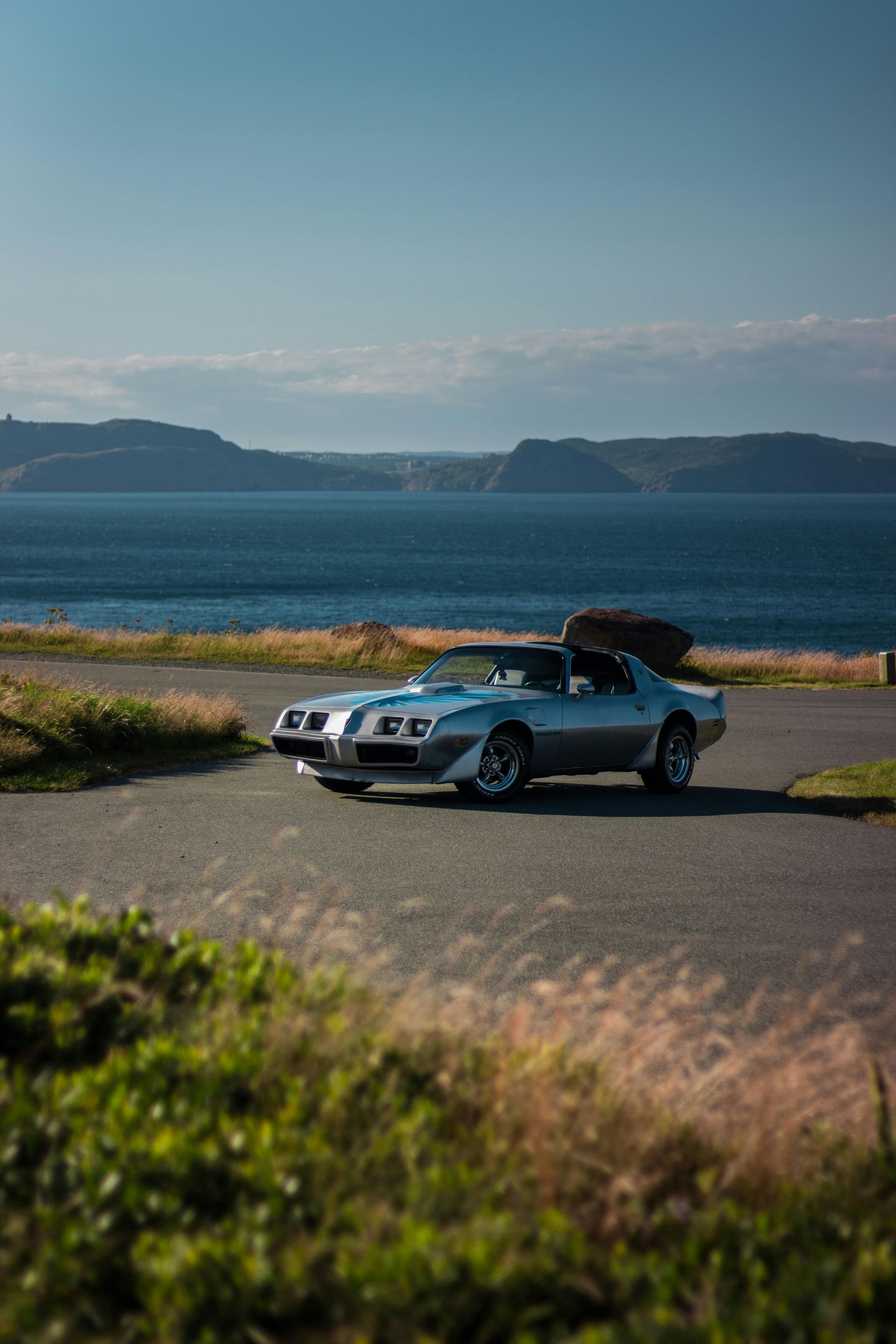A silver car is parked on the side of a road near the ocean.