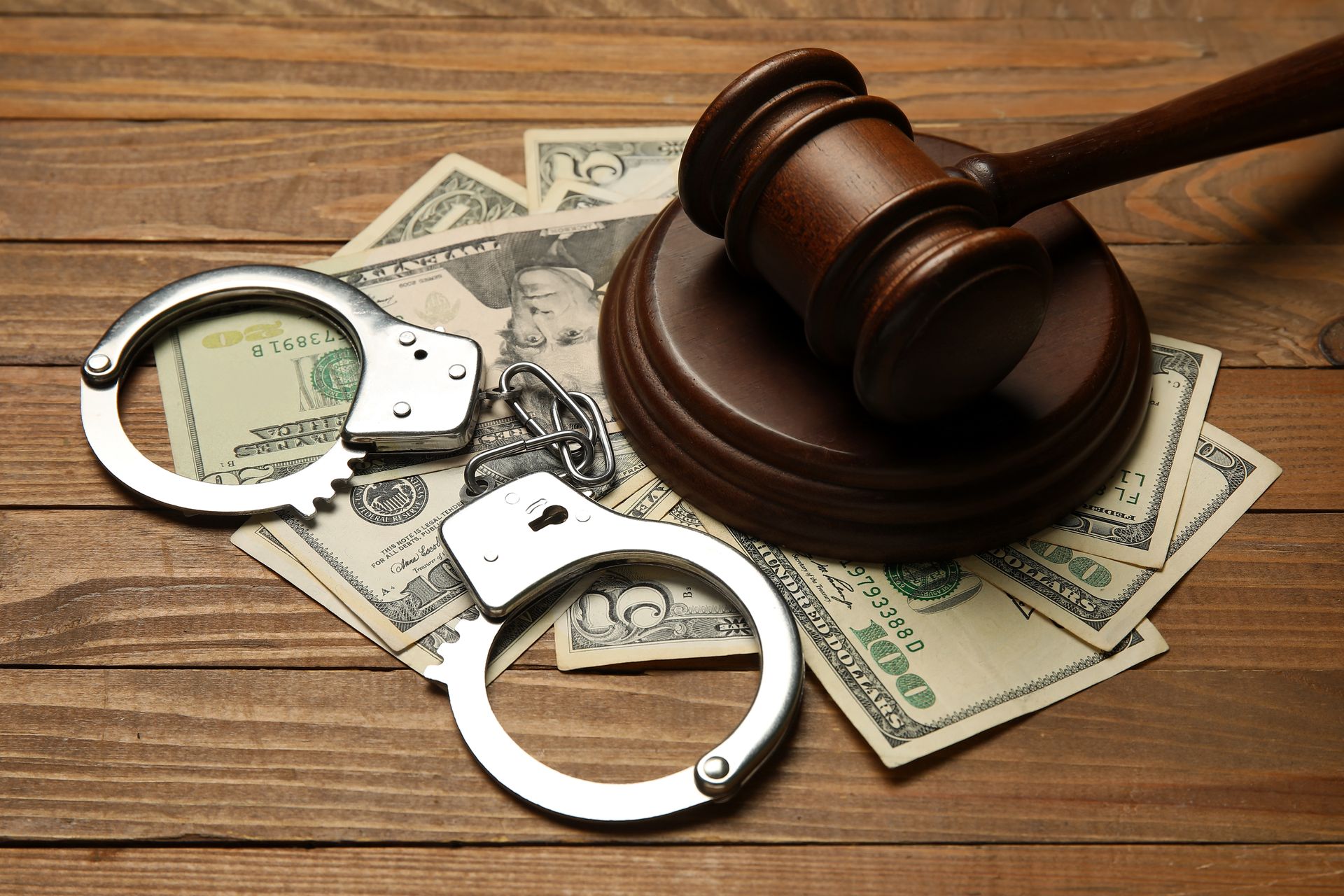 A wooden gavel and a pair of handcuffs are on top of a spread of dollars. A wooden gavel and a pair of handcuffs are on top of a spread of dollars.