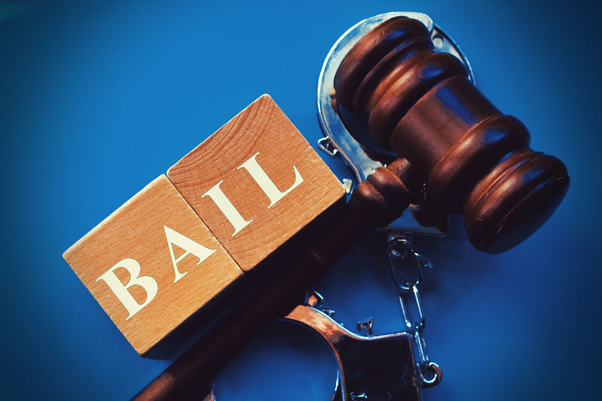 Word “BAIL” composed of wooden cubes with a gavel and handcuffs on a blue background.