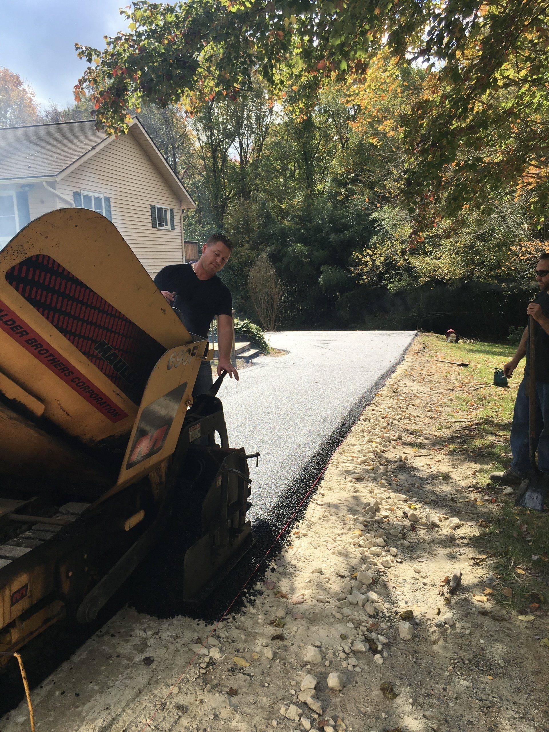 Asphalt paving a driveway; man operates machinery.
