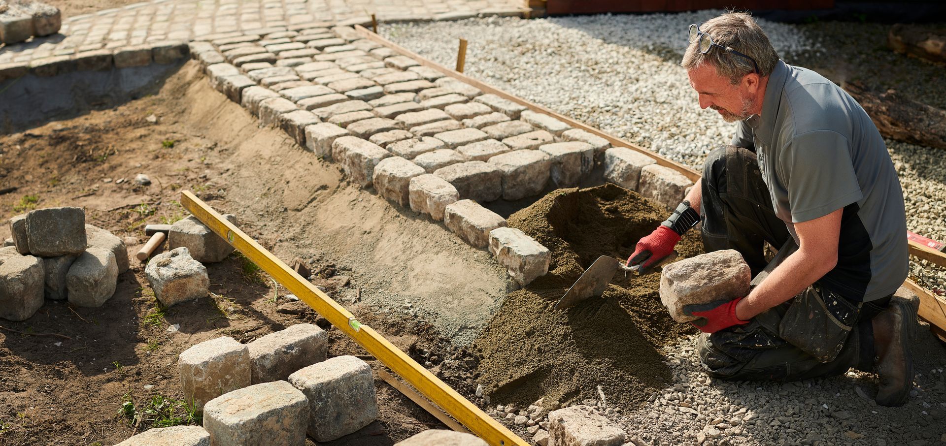 Residential paving contractor laying cobblestone path on a gravel base with level tool.