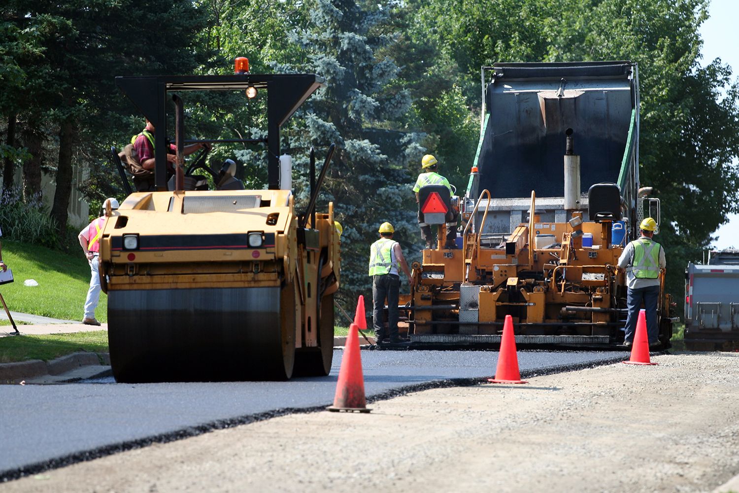 Residential paving contractors use a spreader to lay the first layer of asphalt on a city street.