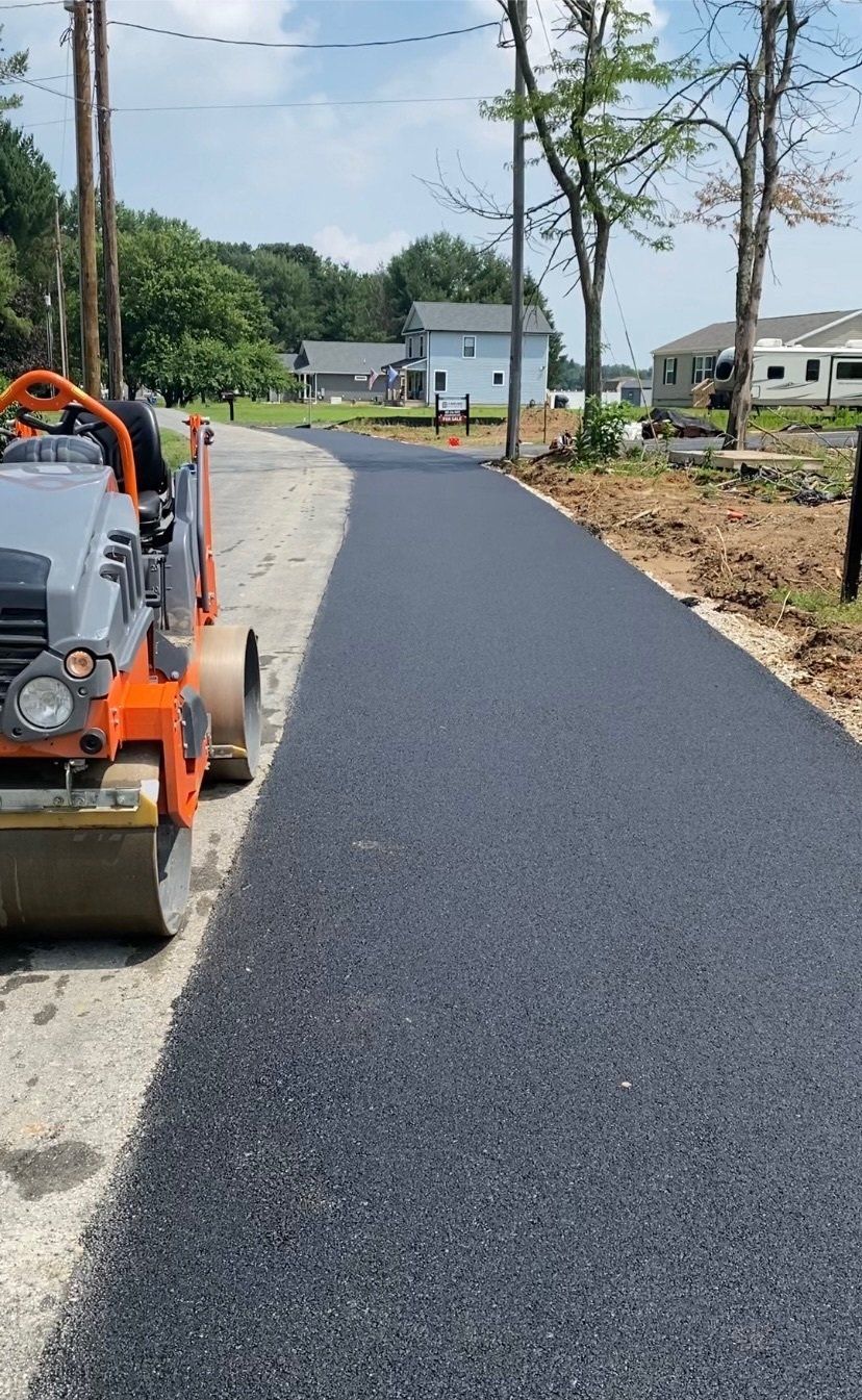 Asphalt paving a narrow road, roller compacting the fresh surface.