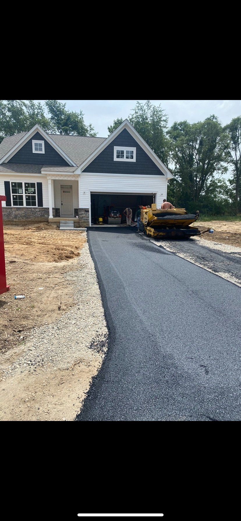 Asphalt driveway being laid in front of a new house, with a yellow construction vehicle visible.