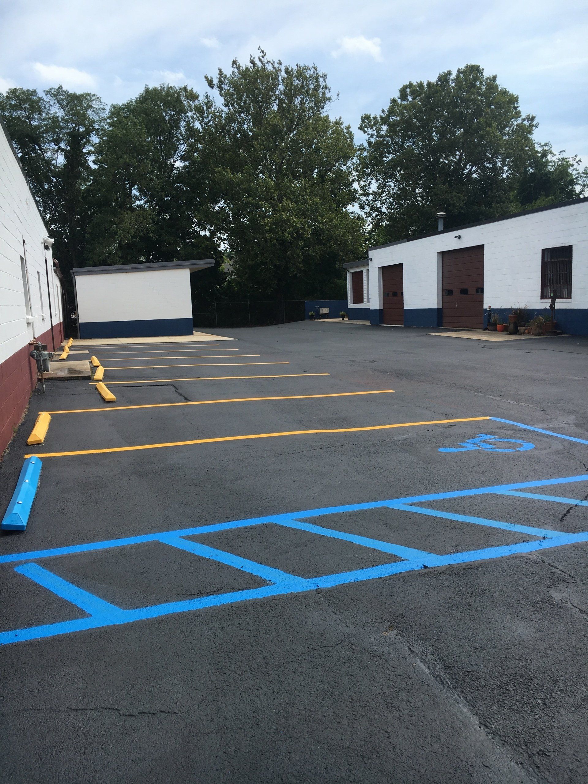 Asphalt parking lot with blue handicap spaces and yellow parking space lines. Buildings and trees in the background.