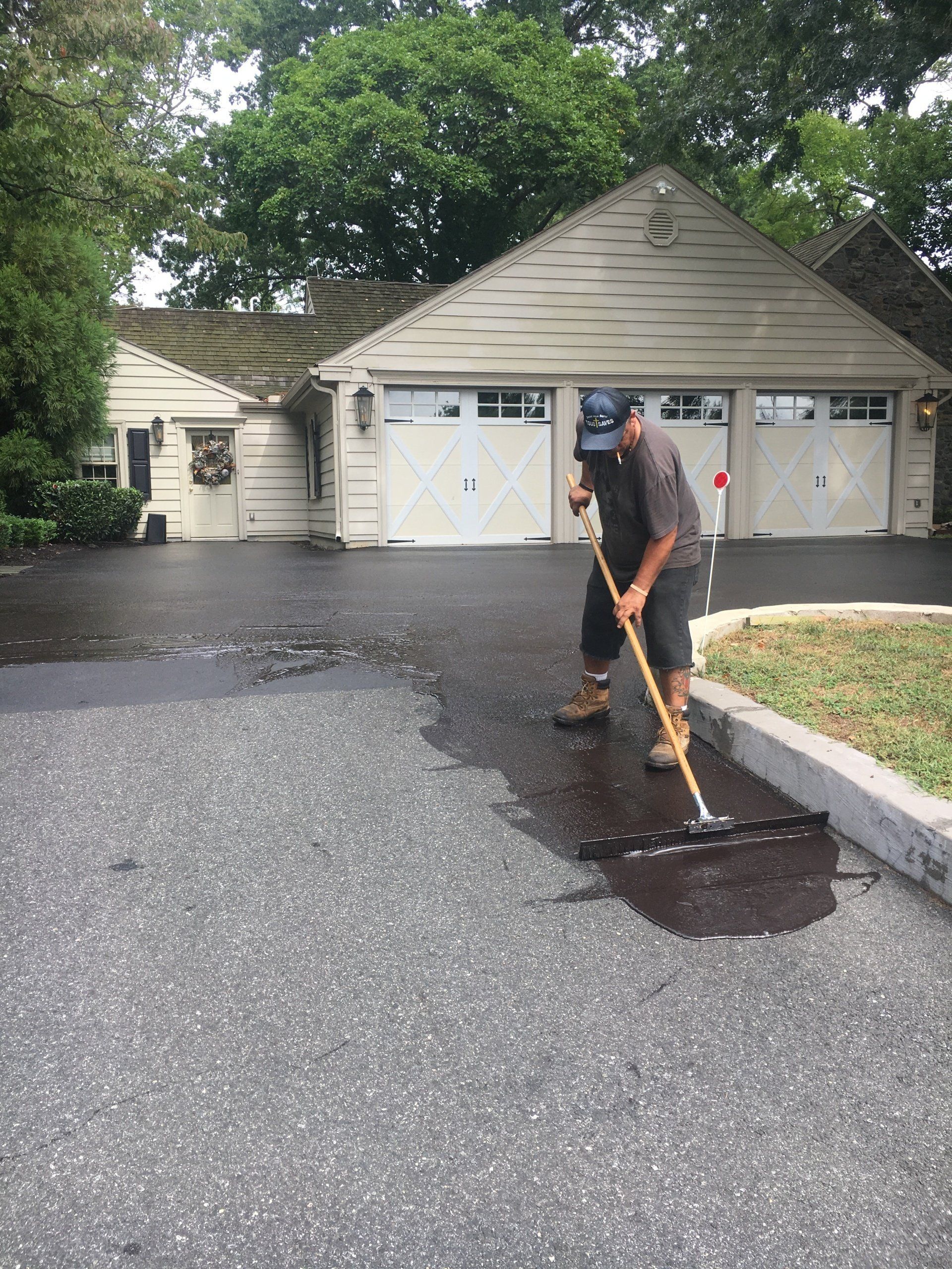 Man spreads asphalt on a driveway in front of a three-car garage.