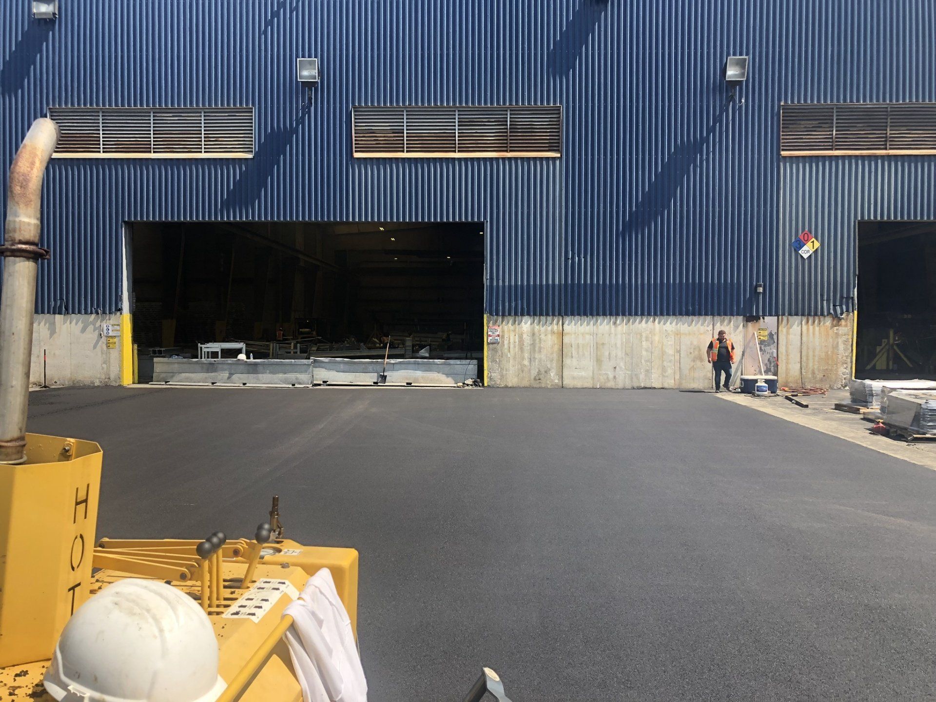 New asphalt in front of a blue industrial building with open loading bay; person standing nearby.