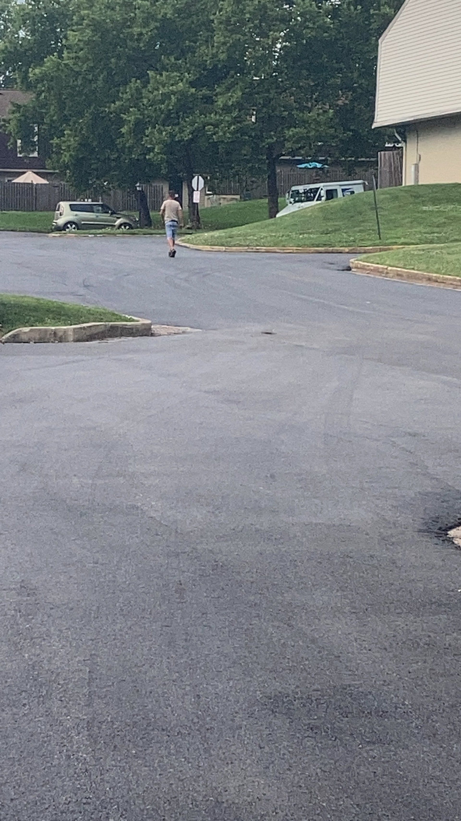 Person riding a scooter down a paved street with a building and trees in the background.