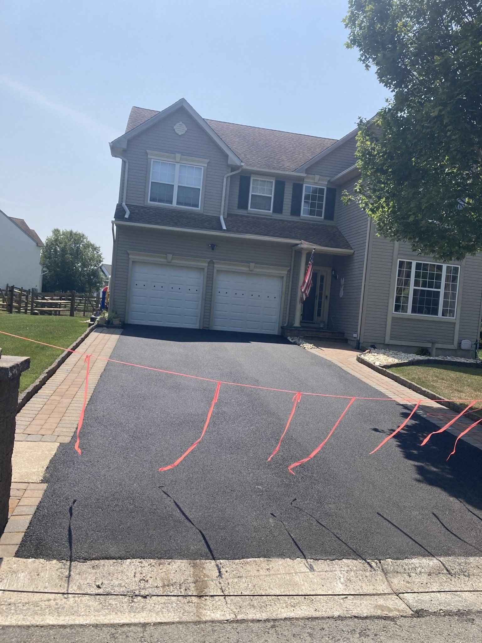 Two-story house with newly paved driveway; cracks with red arrows indicating areas of concern. Sunny day.