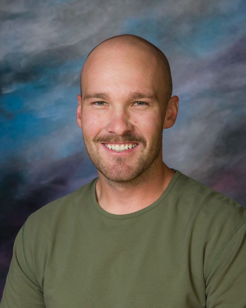 A bald man with a mustache is smiling for the camera while wearing a green shirt.