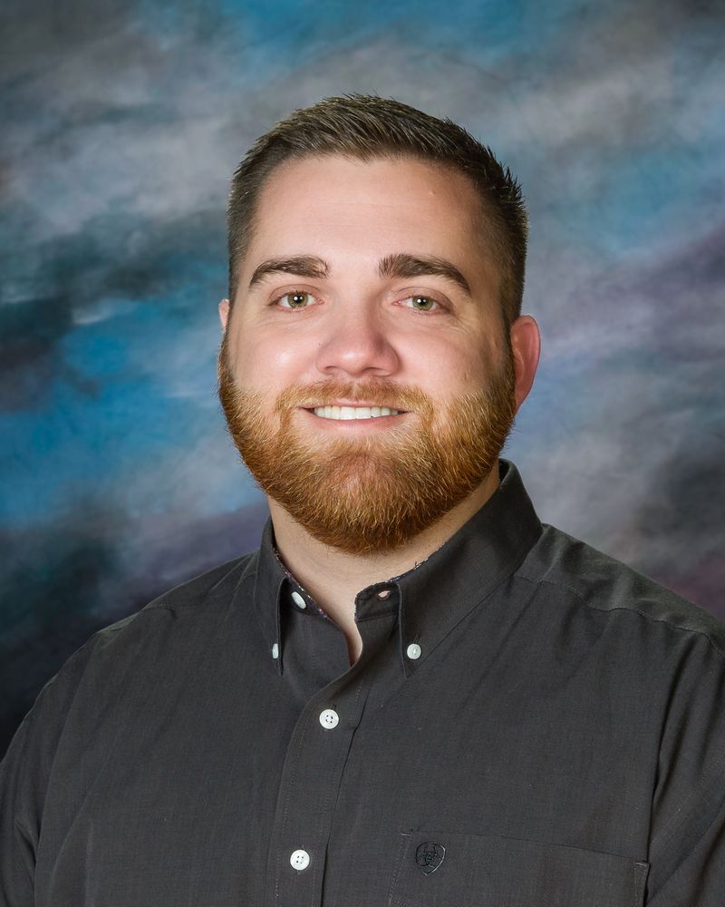 A man with a beard is wearing a black shirt and smiling for the camera.
