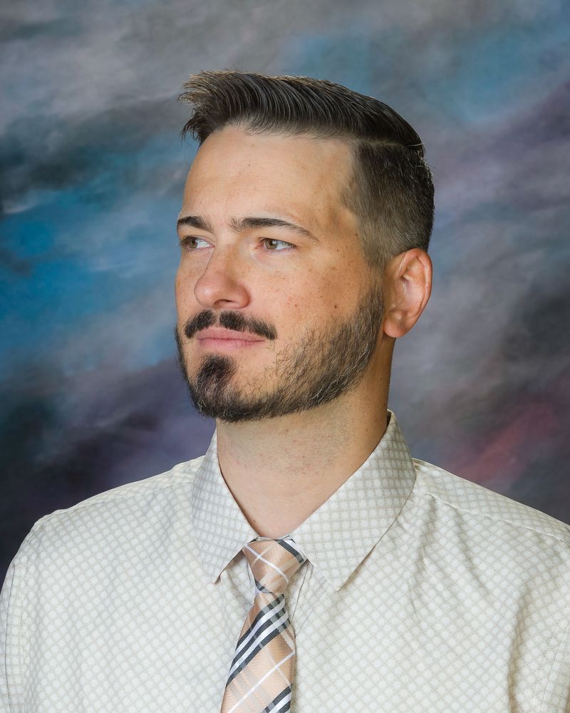 A man with a beard is wearing a white shirt and tie.