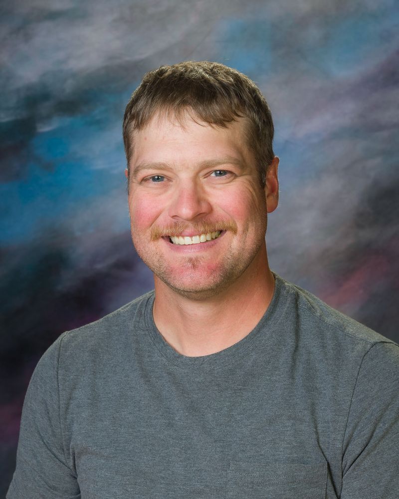 A man in a grey shirt is smiling for the camera.