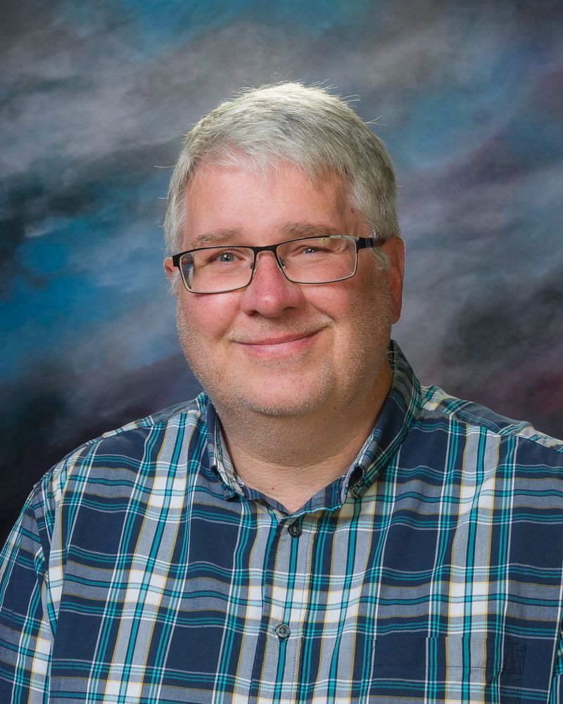 A man wearing glasses and a plaid shirt is smiling for the camera.
