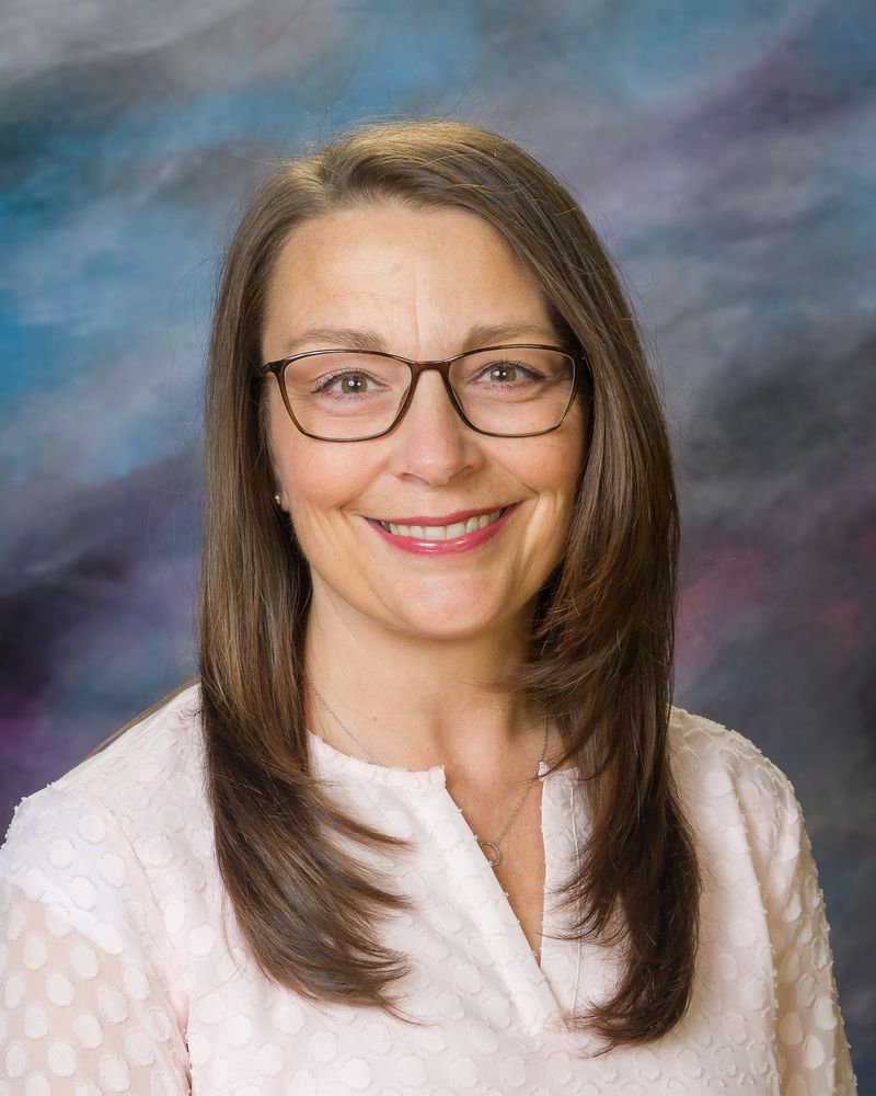A woman wearing glasses and a white shirt is smiling for the camera.