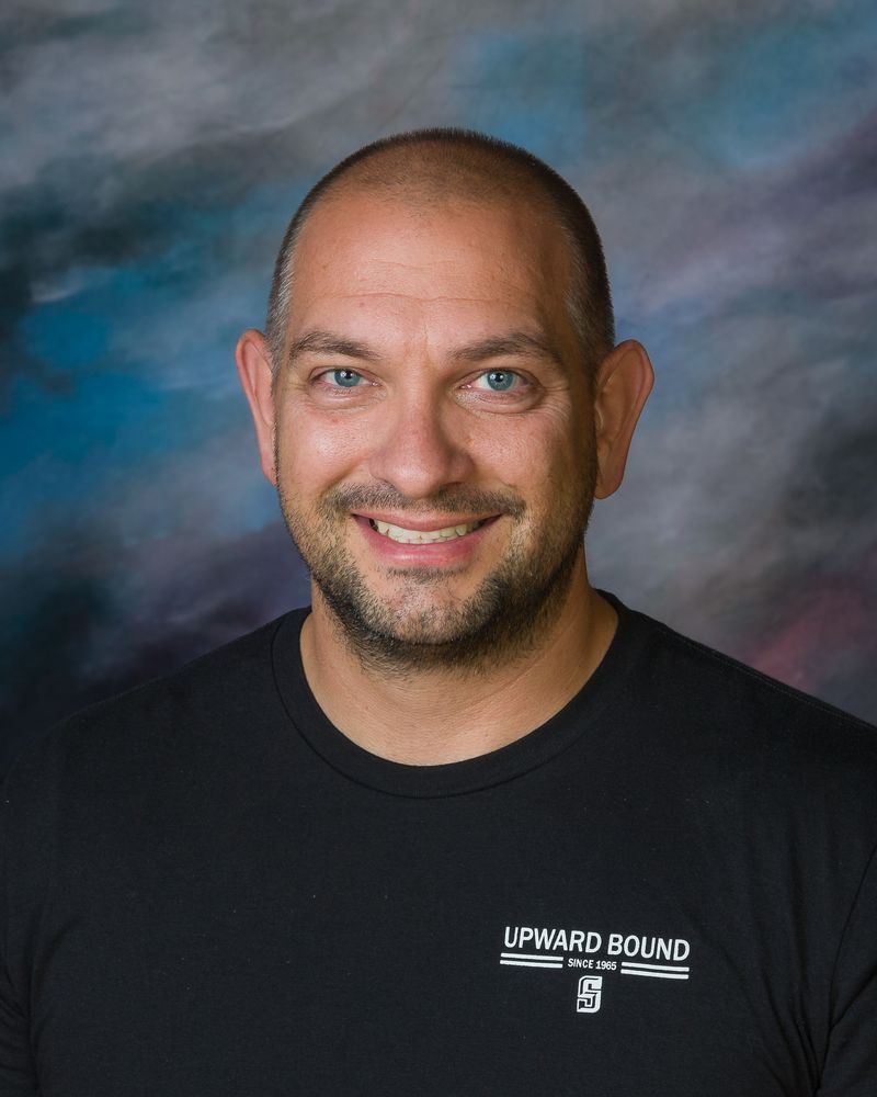 A man with a beard is wearing a black shirt that says upward bound on it.