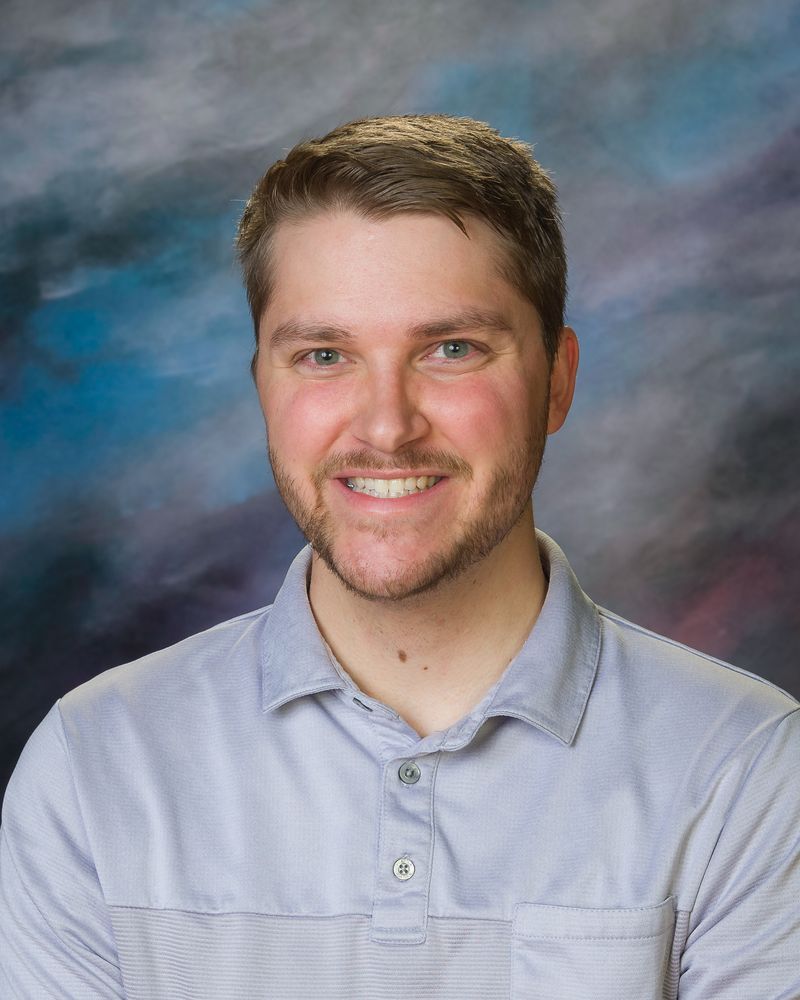 A man with a beard is smiling for the camera while wearing a blue shirt.