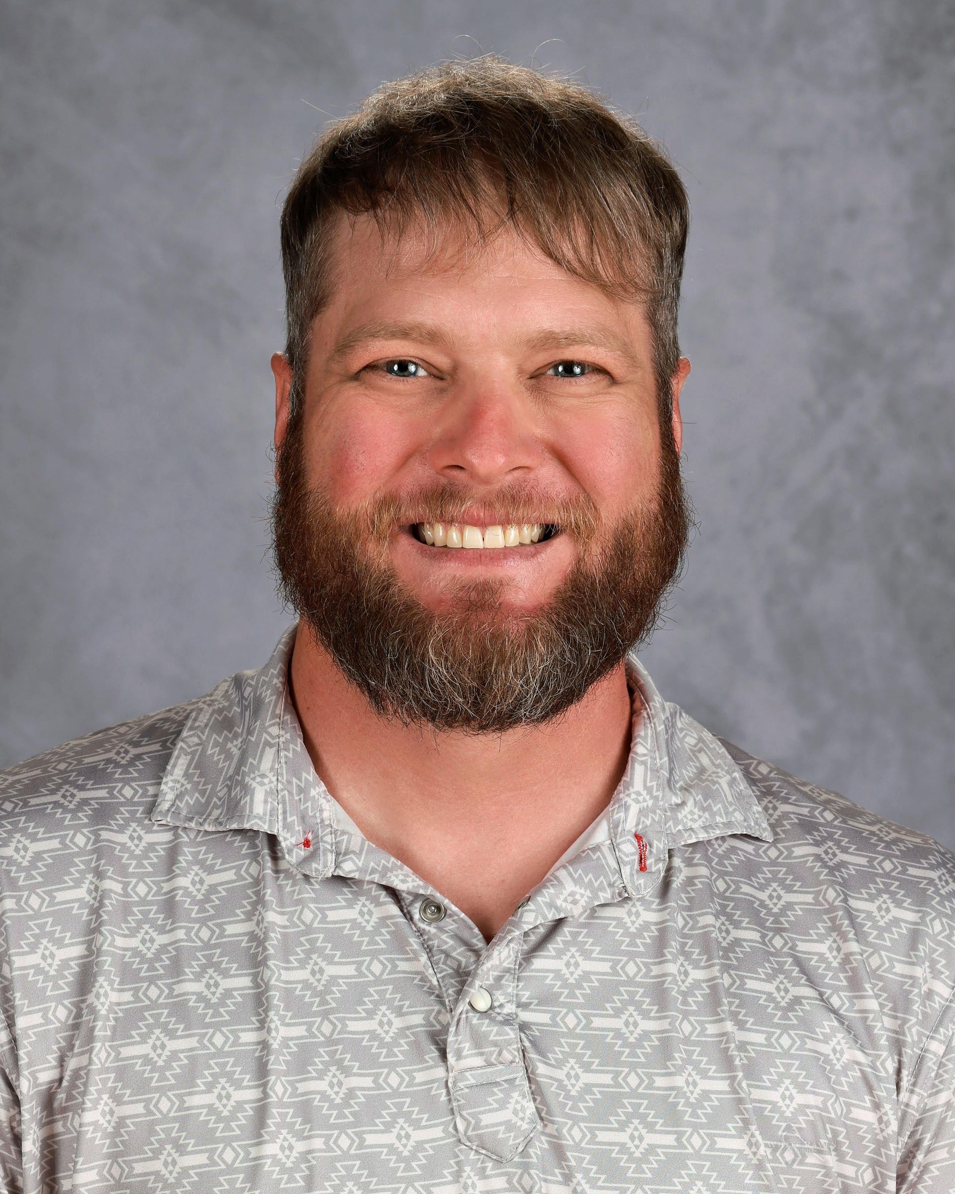Man with beard smiling, wearing patterned gray shirt.