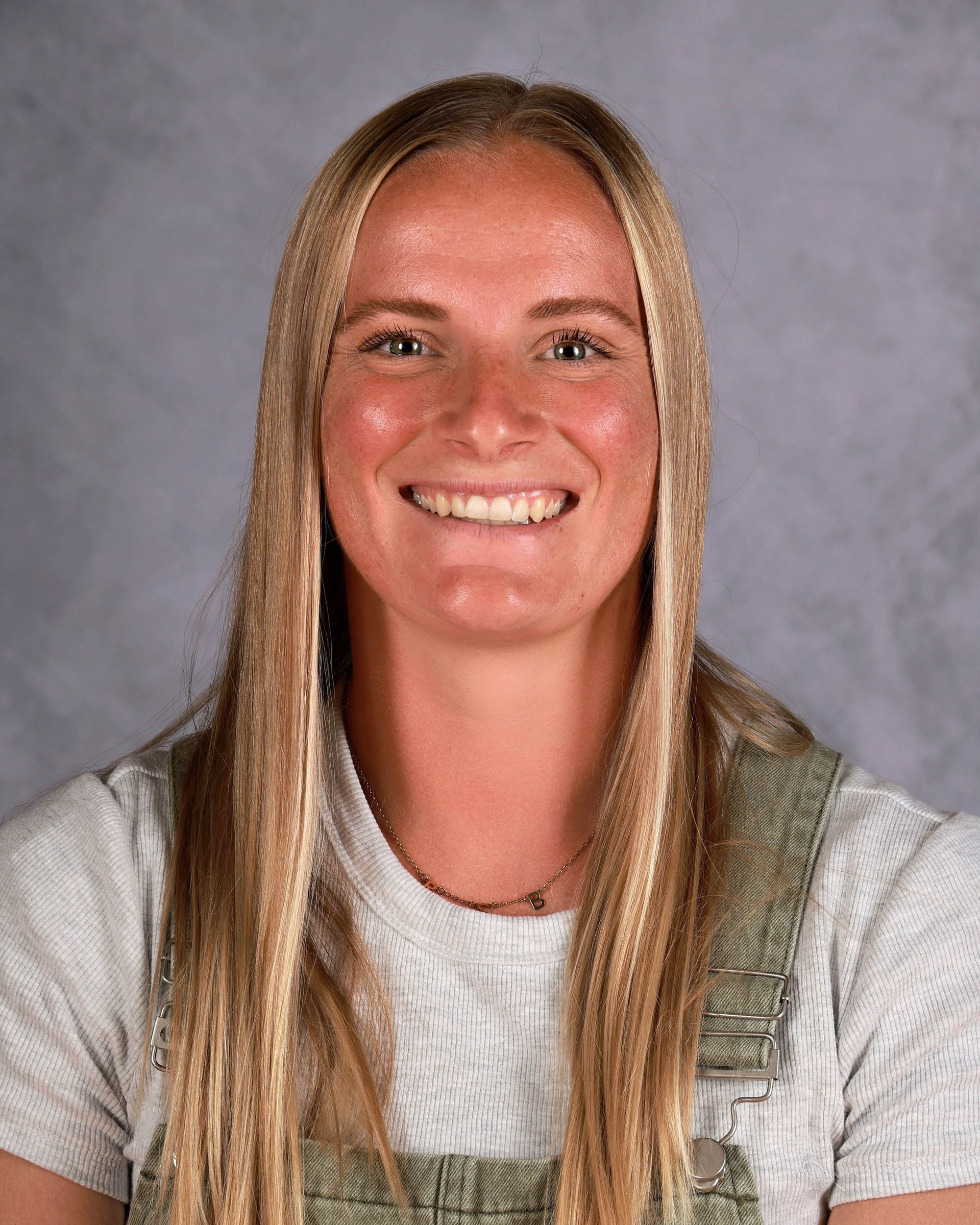 Blonde woman with a big smile, wearing a light-colored shirt and overalls.