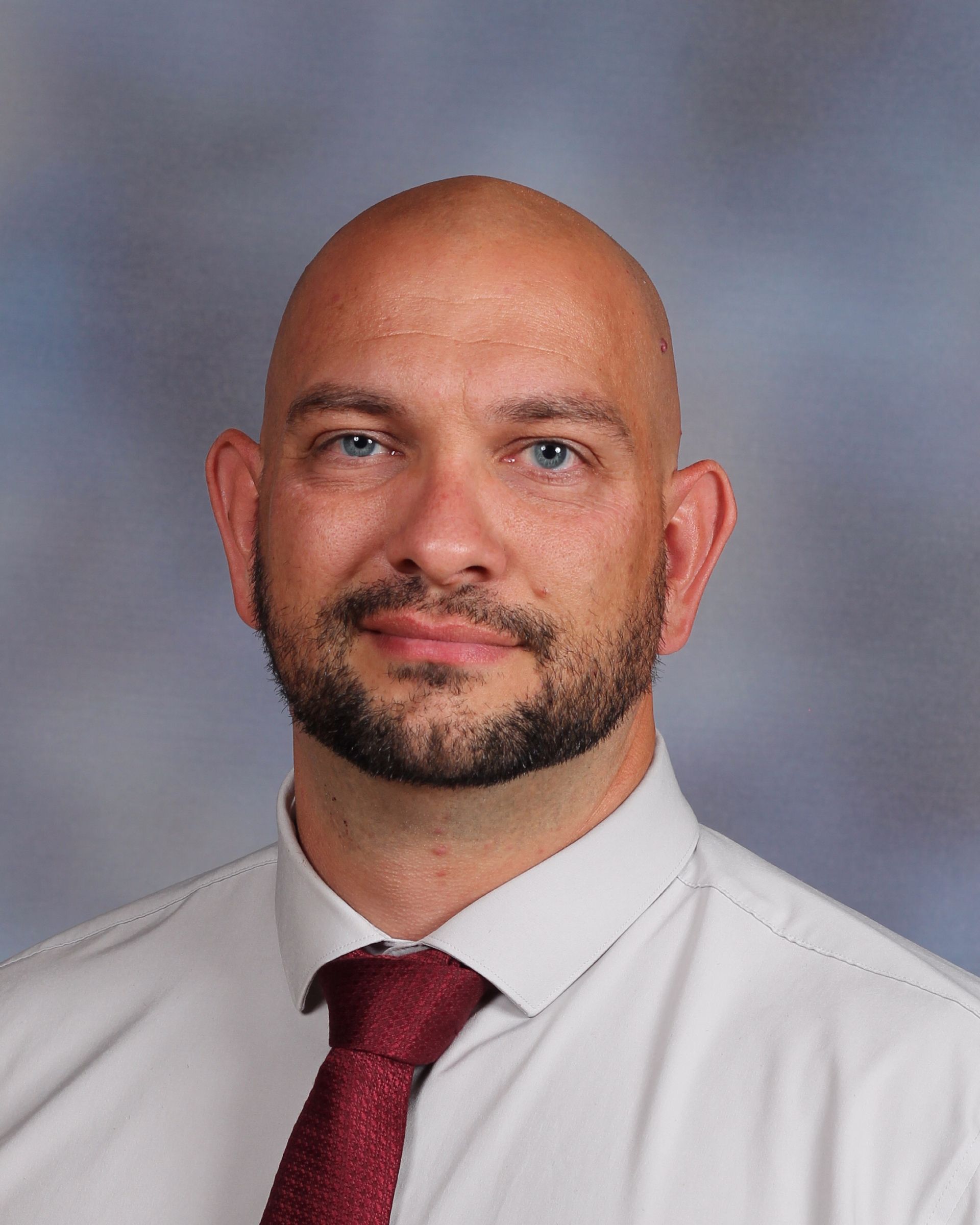 Man with shaved head, beard, and red tie, smiling.
